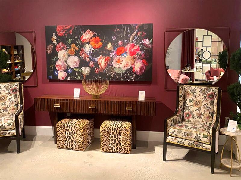 Two chairs in a floral upholstery next to a console table and two ottomans upholstered in leopard print in front of a deep burgandy wall
